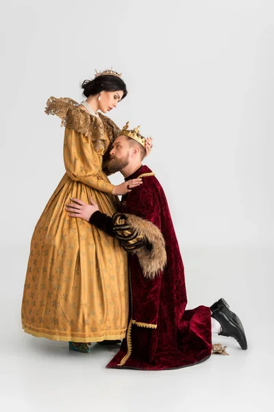Vista lateral del rey con corona abrazando atractiva reina sobre fondo gris - foto de stock