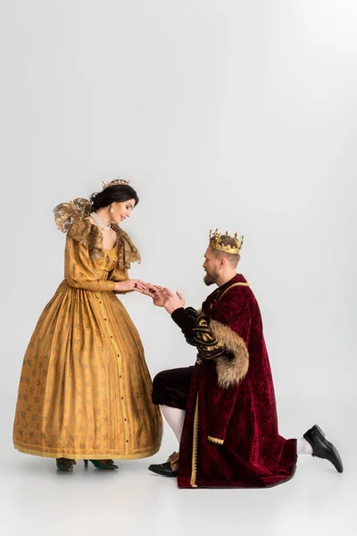 Улыбающаяся королева и король с коронами, держащимися за руки на сером фоне — стоковое фото