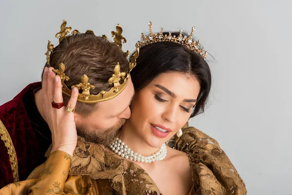 Roi avec couronne étreignant et embrassant jolie reine isolée sur gris — Photo de stock