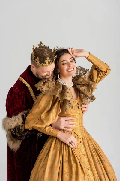 König mit Krone umarmt lächelnde Königin isoliert auf grau — Stockfoto
