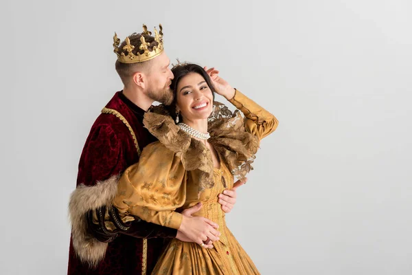 King with crown kissing and hugging smiling queen isolated on grey — Stock Photo