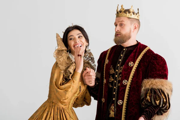 Sonriente reina y rey con coronas cogidas de la mano aisladas en gris - foto de stock