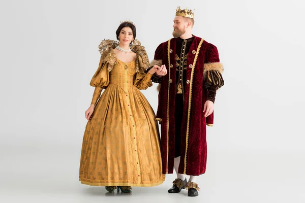 Sonriente reina y rey con coronas cogidas de la mano sobre fondo gris - foto de stock
