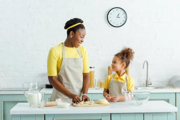 Happy african american mother and daughter sculpting raw dumplings in kitchen — Stock Photo