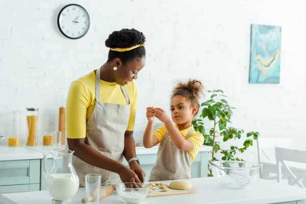 Glücklich afrikanisch-amerikanische Mutter und süße Tochter Modellierung rohe Knödel in der Küche — Stockfoto