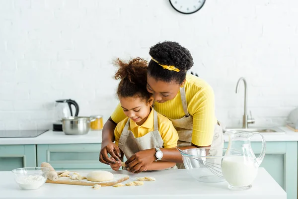 Heureux afro-américain mère près de mignonne fille sculpter boulettes dans la cuisine — Photo de stock