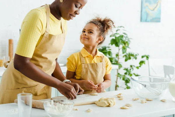 Criança americana africana feliz olhando mãe esculpindo bolinhos na cozinha — Fotografia de Stock