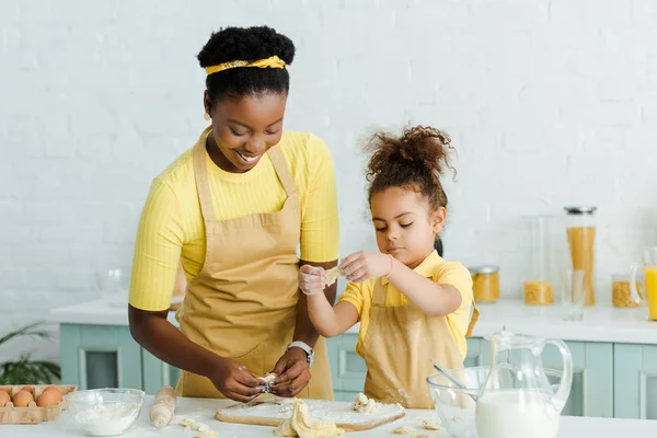 Весела афроамериканська мати і мила дочка в фартухах скульптури сирих пельменів на кухні — стокове фото