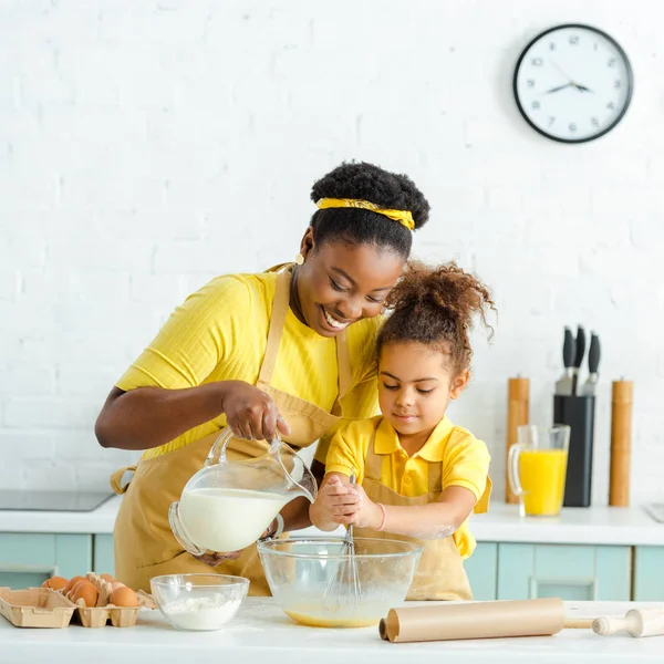 Fröhliche afrikanisch-amerikanische Mutter gießt Milch in Schüssel neben entzückendem Kind — Stockfoto