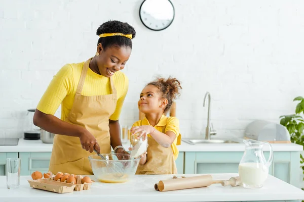 Süßes afrikanisches amerikanisches Kind schaut Mutter an, während es Schüssel mit Mehl hält — Stockfoto