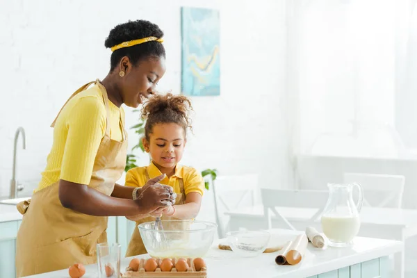 Entzückendes afrikanisch-amerikanisches Kind und fröhliche Mutter beim Kochen in der Küche lächelnd — Stockfoto