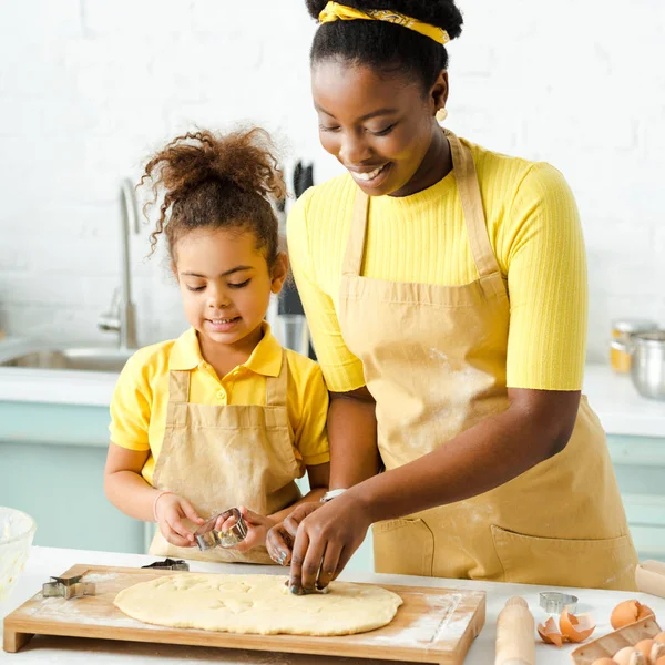 Entzückendes afrikanisch-amerikanisches Kind und glückliche Mutter mit Ausstechformen in der Nähe von rohem Teig — Stockfoto