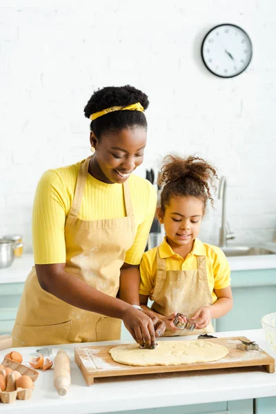 Niño afroamericano y feliz madre sosteniendo cortadores de galletas cerca de masa cruda - foto de stock