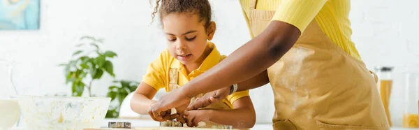 Plano panorámico de lindo afroamericano niño y madre sosteniendo cortadores de galletas cerca de masa cruda - foto de stock