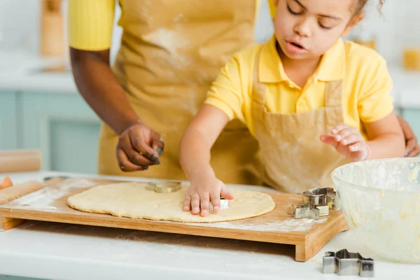 Vista ritagliata della madre afro-americana e adorabile figlia che tiene tagliabiscotti vicino alla pasta — Foto stock