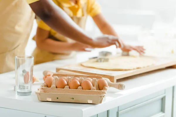 Foco seletivo de ovos frescos perto de mãe e filha afro-americana na cozinha — Fotografia de Stock