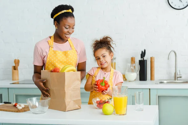 Cheerful african american mother looking at daughter with bell peper — Stock Photo