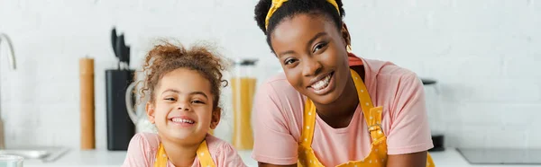 Panoramic shot of happy african american mother and cute daughter looking at camera — Stock Photo