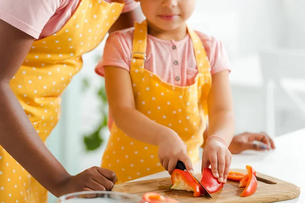 Cropped view of african american kid cutting bell pepper near mother — Stock Photo