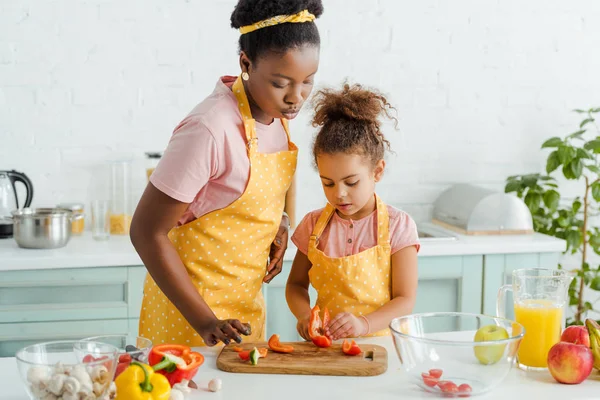 African american mother and daughter looking at bell pepper on cutting board — Stock Photo