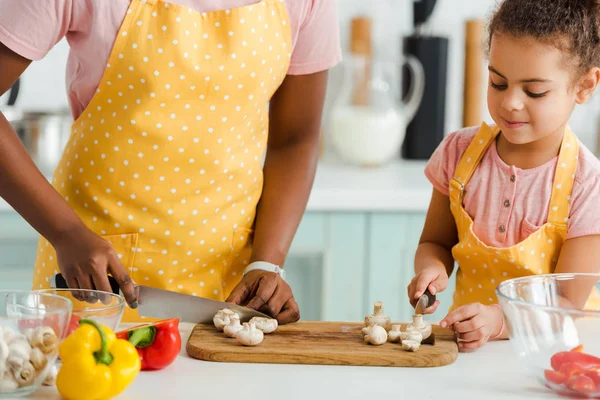 Vista recortada de la madre afroamericana y su hija cortando setas - foto de stock