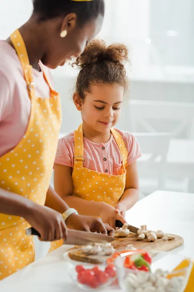 Messa a fuoco selettiva di felice bambino africano americano e madre taglio funghi — Foto stock