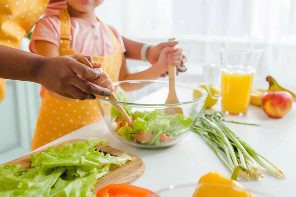 Cropped view of african american mother and daughter mixing fresh salad — Stock Photo