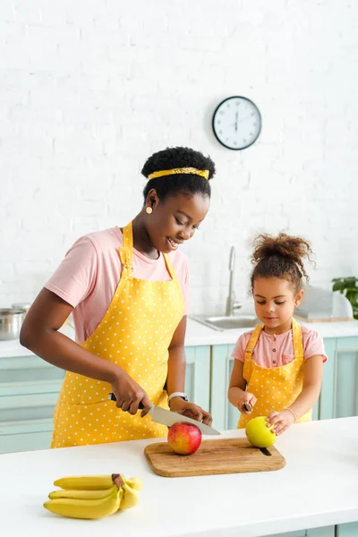 Happy african american mother and cute daughter cutting apples — Stock Photo
