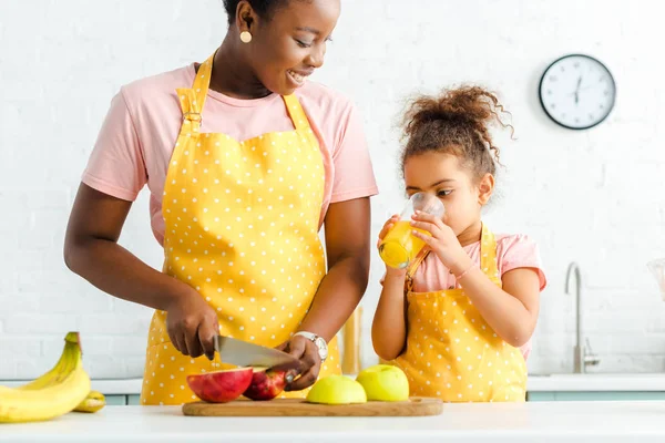 Happy african american mother looking at cute daughter drinking fresh orange juice — Stock Photo