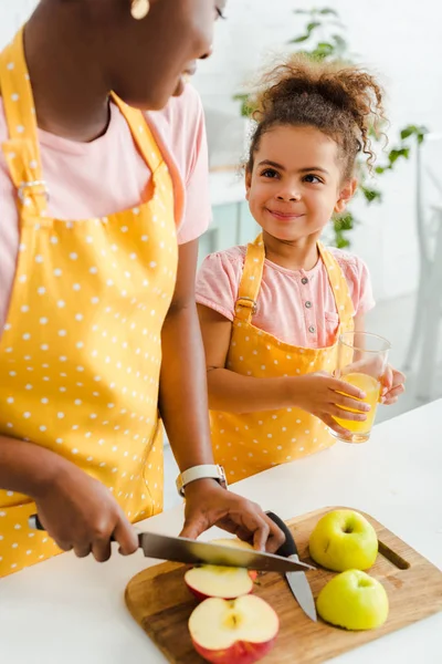 Happy african american kid holding glass with orange juice and looking at mother — Stock Photo