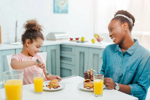 Heureuse mère afro-américaine regardant fille près de crêpes savoureuses — Photo de stock