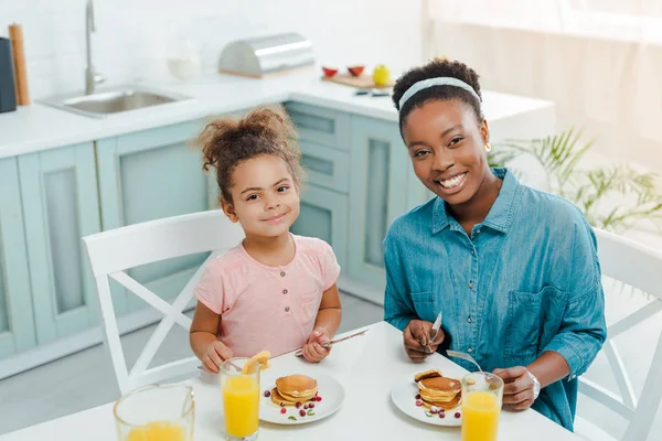 Felice afroamericana madre e figlia guardando la fotocamera vicino gustosi pancake — Foto stock