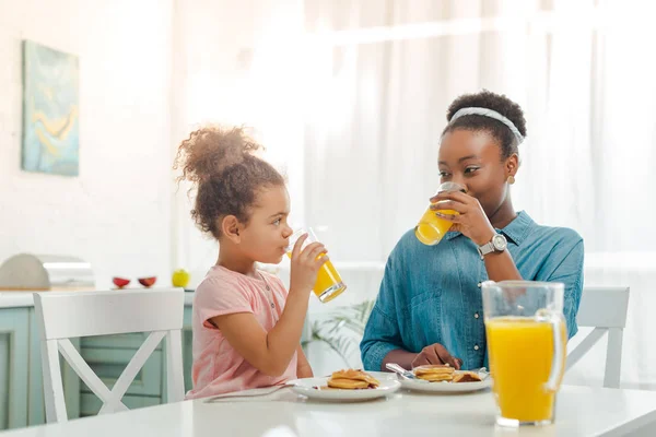 Афроамериканська мати і дочка п'ють апельсиновий сік біля смачних млинців — стокове фото