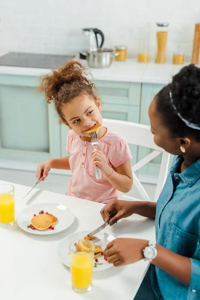 African american mother looking at daughter eating tasty pancakes — Stock Photo