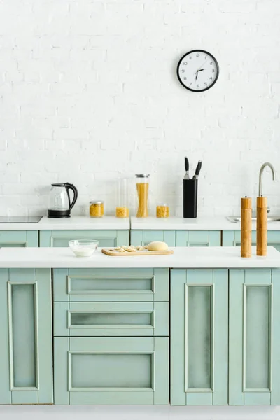 Raw dumplings on wooden cutting board near bowl with flour in kitchen — Stock Photo