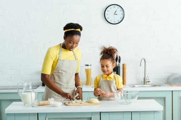 Madre e hija afroamericana esculpiendo albóndigas cerca de la jarra con leche en la cocina - foto de stock