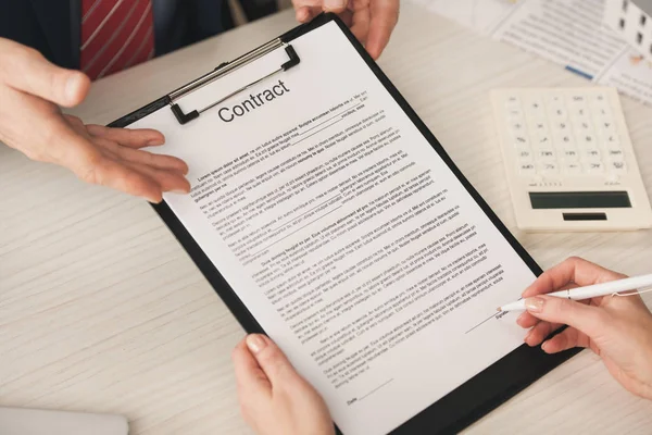 Ausgeschnittene Ansicht eines Agenten, der mit der Hand auf Klemmbrett mit Vertragsbeschriftung in der Nähe einer Frau zeigt, die einen Stift hält — Stockfoto