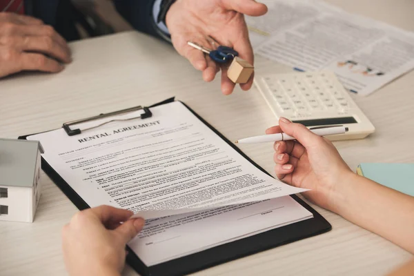 Cropped view of woman holding pen near clipboard with rental agreement lettering and agent with keys — Stock Photo