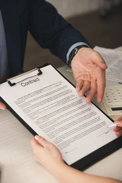 Ausgeschnittene Ansicht eines Agenten, der mit der Hand auf Klemmbrett mit Vertragsbeschriftung zeigt, in der Nähe einer Frau mit Stift — Stockfoto