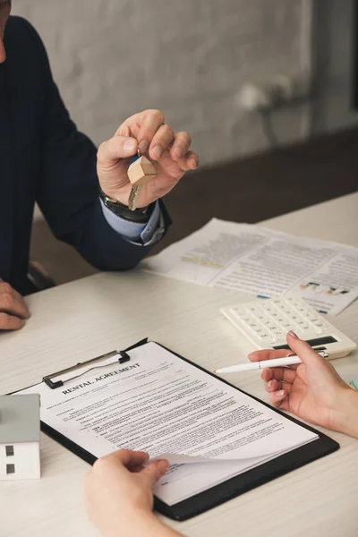 Vista recortada de la mujer que sostiene la pluma cerca del portapapeles con letras de acuerdo de alquiler y corredor con llaves — Stock Photo