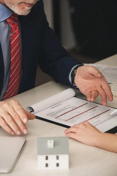 Vue recadrée de l'agent barbu pointant avec la main au presse-papiers avec lettrage d'assurance près de la femme — Photo de stock