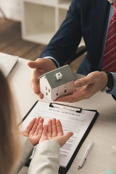Cropped view of agent holding house model near woman with cupped hands — Stock Photo
