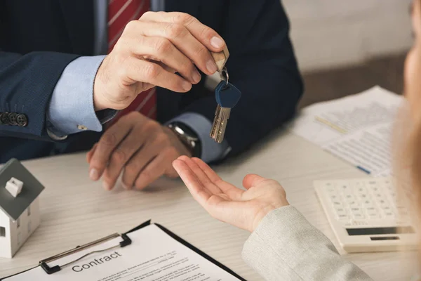 Vista recortada de agente inmobiliario dando llaves a la mujer con la mano ahuecada cerca del contrato - foto de stock