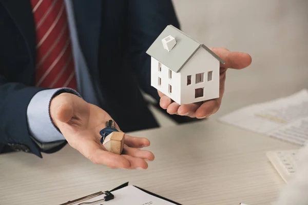 Vista recortada de bienes raíces con llaves y modelo de casa de cartón en la oficina - foto de stock