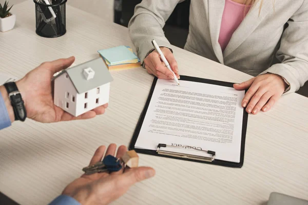 Cropped view of man holding keys and house model near woman signing contract — Stock Photo