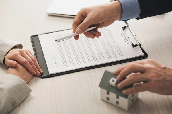 Abgeschnittene Ansicht eines Agenten mit Stift und anrührendem Hausmodell in der Nähe von Frau und Vertrag — Stockfoto