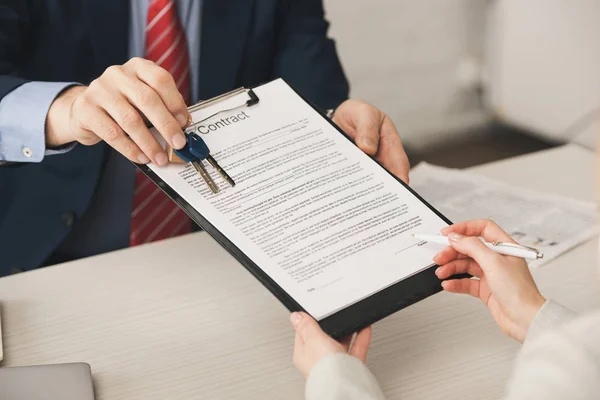 Vista recortada de la mujer que sostiene la pluma cerca del portapapeles con letras de contrato y agente inmobiliario con llaves — Stock Photo