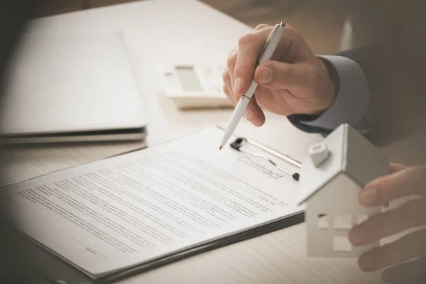 Cropped view of agent holding pen and touching house model near clipboard with contract lettering — Stock Photo