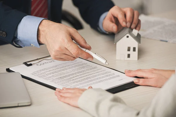 Cropped view of agent giving pen to woman while touching house model — Stock Photo