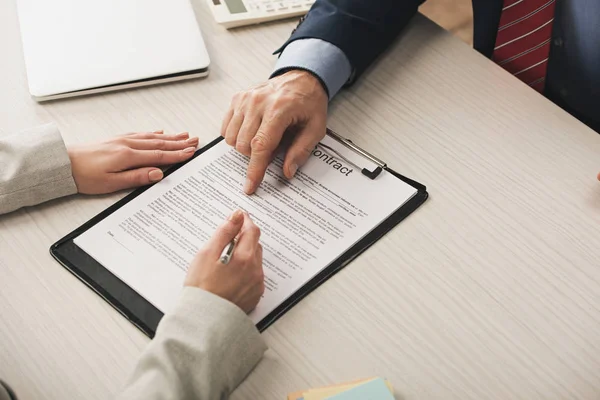 Cropped view of realtor pointing with finger at clipboard with contract lettering near client — Stock Photo